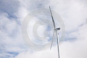 Ground low view on wind propeller turbine, blue sky, and clouds.