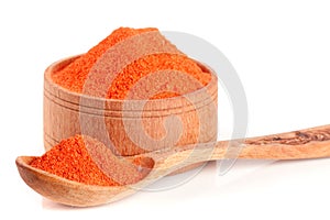 Ground paprika in a wooden bowl with a spoon isolated on a white background