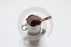 Ground roasted coffee sprinkled on white background and white coffee cup close up close up