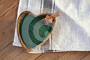 Ground Spirulina in bowl on textile background, top view on hear