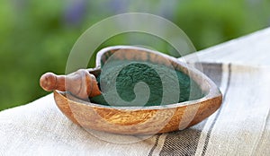 Ground Spirulina in bowl on textile background, top view on hear