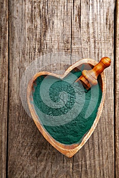 Ground Spirulina in heart shape bowl on wood background, top view