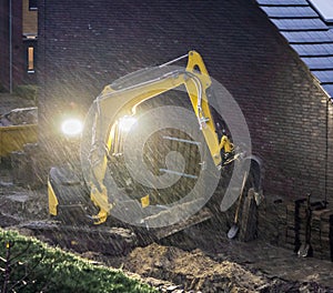 Ground worker working at night in bad rainy weather, constructing a garden in the evening