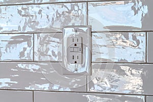 Grounded outlet with three slot receptacle against the white tile wall of home