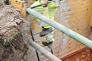Groundworker builder using steps ladder to get out of deep drainage eaxcavation trench support box. Builder going up using