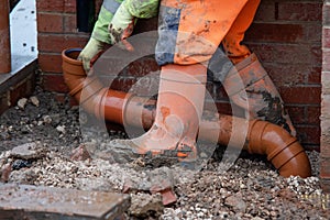 Groundworker fitting plastic drainage pipe to connect down pipe from the roof of new build house to underground drainage