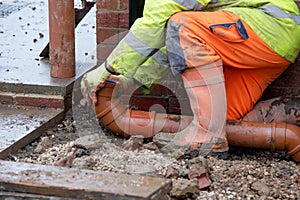 Groundworker fitting plastic drainage pipe to connect new build house to the underground drainage network