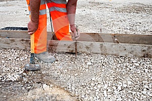 Groundworker making shutter for concrete to form a base for kerb using scaffold boards and steel road pins during new road