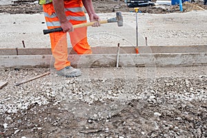 Groundworker making shutter for concrete to form base for kerb using scaffold boards and steel road pins during new road