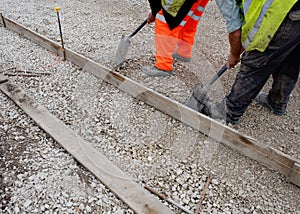 Groundworker in orange safety hi vis trousers fixing a timber along string line with steel pin to form a kerb riser