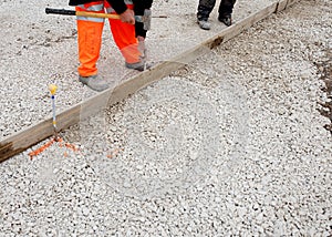 Groundworker in orange safety hi vis trousers fixing a timber along string line with steel pin to form a kerb riser