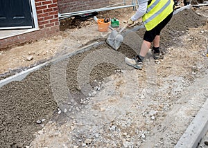 Groundworker placing and levelling with the shovel a semi-dry concrete around edging kerb during footpath construction photo