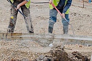 Groundworker placing wet concrete inside formwork during roadworks and new road construction