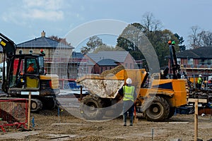 Groundworker waiting for dumper to be loaded by excavator and houses under construction