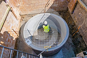 Groundworker working in new built deep manhole during drainage works marking for pipes position