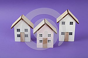 a group of 3 miniature houses lined up on a bright purple background