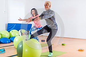 Group of active cheerful sporty women doing single leg squats with balance ball training indoors in gym