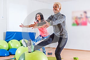 Group of active cheerful sporty women doing single leg squats with balance ball training indoors in gym