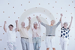 Group of active elderly people holding hands up and enjoying meeting