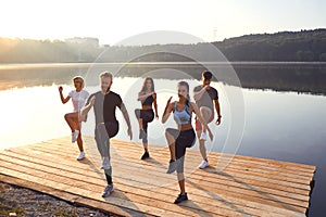 A group of active people do exercises in the park near the lake.