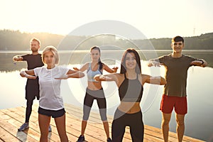 A group of active people do exercises in the park near the lake.