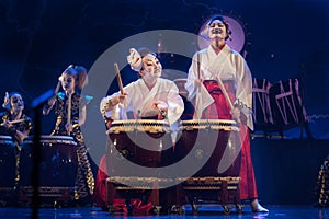 Group of actresses in traditional kimono and fox masks drum taiko drums on the stage