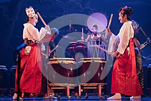 Group of actresses in traditional white and red kimono and fox masks drum on the stage