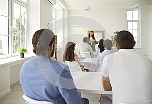 Group of adult students sitting at desks in classroom and listening to college teacher