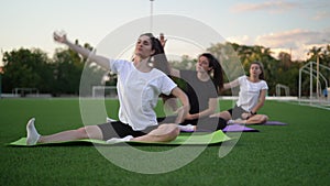 Group of adult women doing yoga in nature. Fitness stretching workout sitting on the grass in the park. Fitness, sport