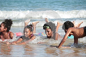 Group African kids in swimsuit have fun together on beach, boys and girls with black curly hair lying down in line at tropical sea