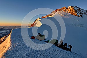 Group alpinists in base camp on snowy peak places tent at sunset, pass Mirali, 5300, Fann, Pamir Alay, Tajikistan