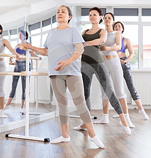 Group of amateurs of different ages practice ballet moves in classical dance class