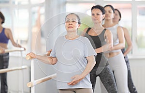 Group of amateurs of different ages practice ballet moves in classical dance class