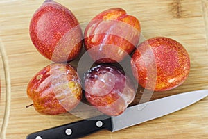 Five Amigo Pluots on a Wood Chopping Board with a Knife photo