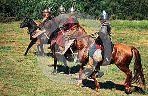 Group of ancient equestrians in historical costumes are reconstructed. The medieval armored knights are on the horses