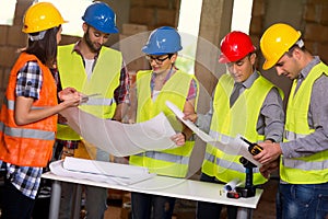 Group of architects and construction workers look at blue print