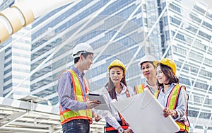 Group of asian adult civil engineers wearing safety helmet, discussing, holding papers of building construction project plan while