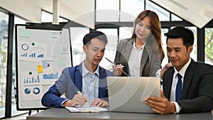 Group of Asian businesspeople looking at laptop screen, planning a new project together