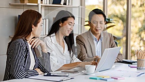 Group of Asian businesspeople working communicating and looking at laptop screen while sitting on a desk together. Concentration