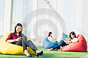 Group of Asian college student or business colleague using smartphone sit together in modern office or university campus