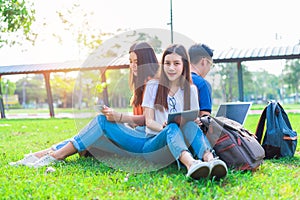 Group of Asian college student using tablet and laptop on grass field at outdoors. Technology and Education learning concept.