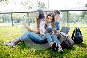 Group of Asian college student using tablet and laptop on grass field at outdoors. Technology and Education learning concept.