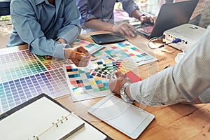 Group of Asian designers brainstorming working together with colleagues and color swatches in co-working workplace