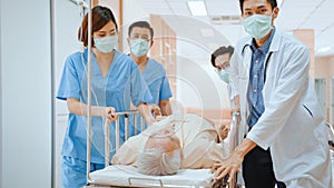 Group of Asian emergency doctor and nurse team wear face mask, push emergency stretcher, transport senior patient in hospital