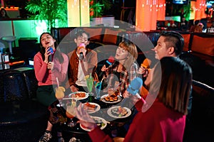 Group of asian friends having fun and singing songs at karaoke club