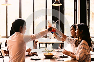 Group of Asian happy and smiling young man and women holding an alcoholic cocktail for toasting in restaurant against sunset.