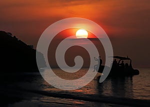 A group of Asian men are sitting on a boat looking at the sunset, the beautiful red sky. Right in front of the beach