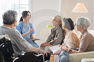 Group of Asian senior people sit in a circle in a nursing home and listen to nurse during a group elderly therapy session.
