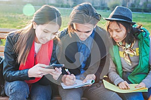 Group of Asian teenage students schoolchildren sitting on a bench in the park and preparing exams