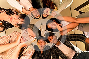 a group of Asian teenagers forming a circle and looking down with funny faces in an old room